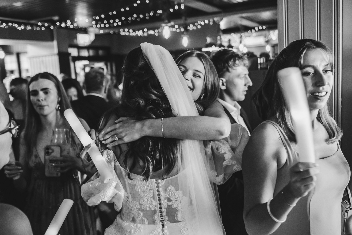 People dancing and celebrating at a lively wedding reception under string lights and decorations.