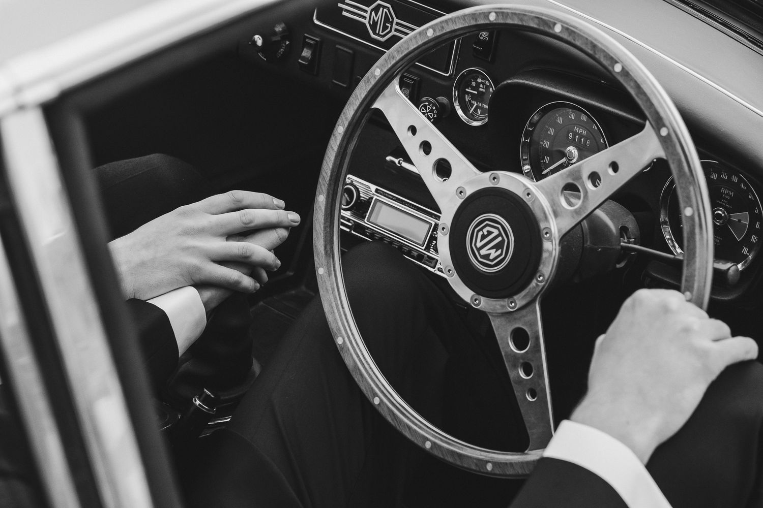 Close-up view of hands gripping a classic car steering wheel with chrome details and wooden trim.