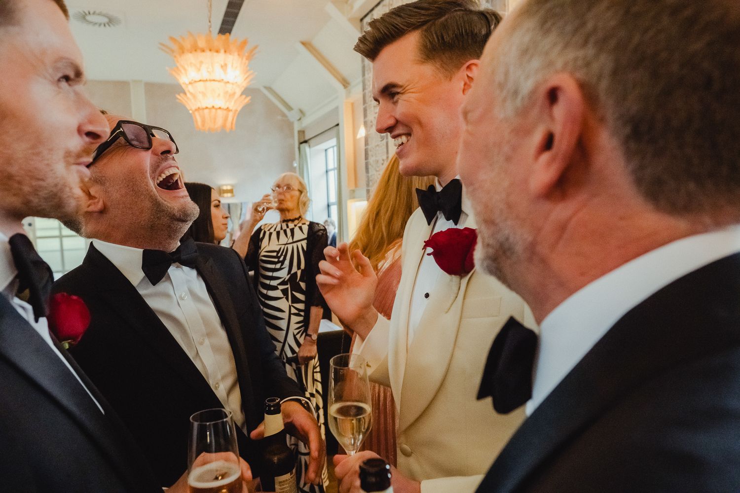 Well-dressed guests in formal attire laugh and socialize while holding champagne glasses at an elegant event.
