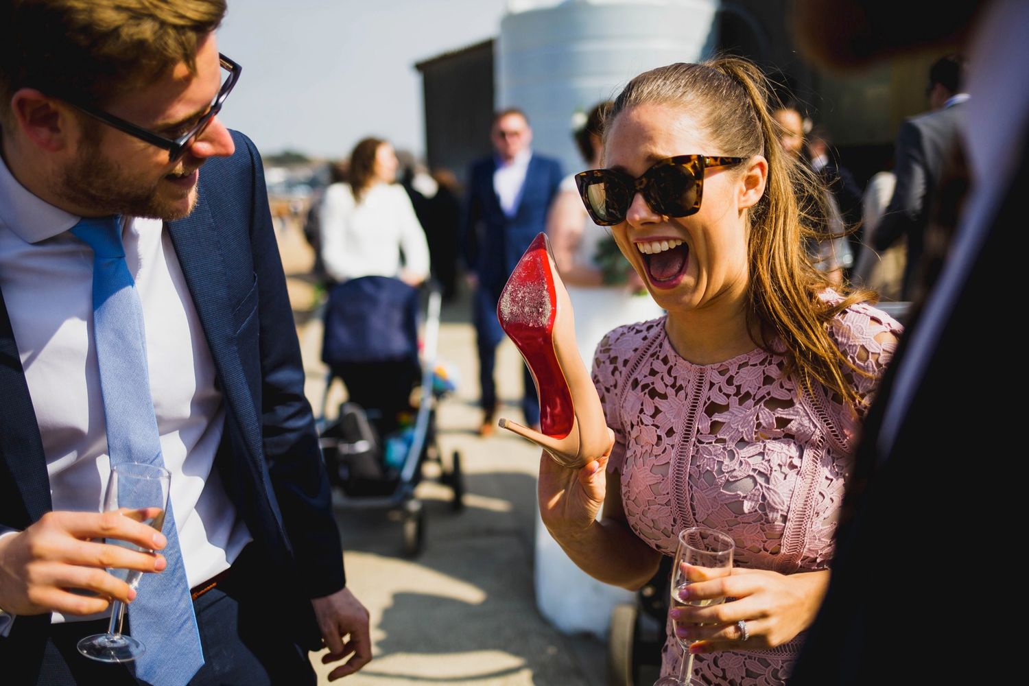 Stylishly dressed guests chatting and holding drinks at a sunny outdoor event.
