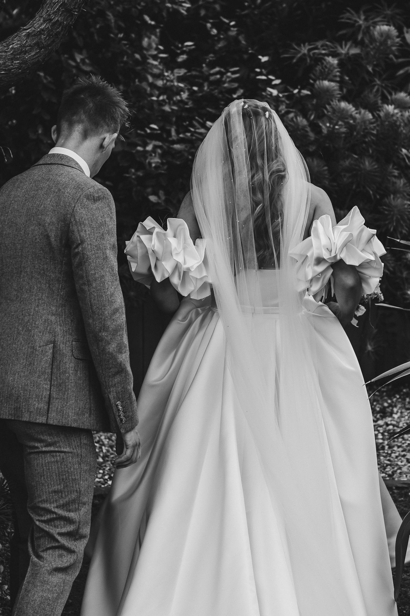 A black and white wedding photo sequence showing the back details of a bride's elegant white gown with ruffled accents.