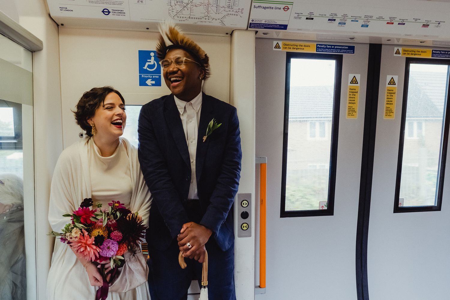 A joyful couple shares a candid moment of laughter in a bright hallway with framed photos on the wall.