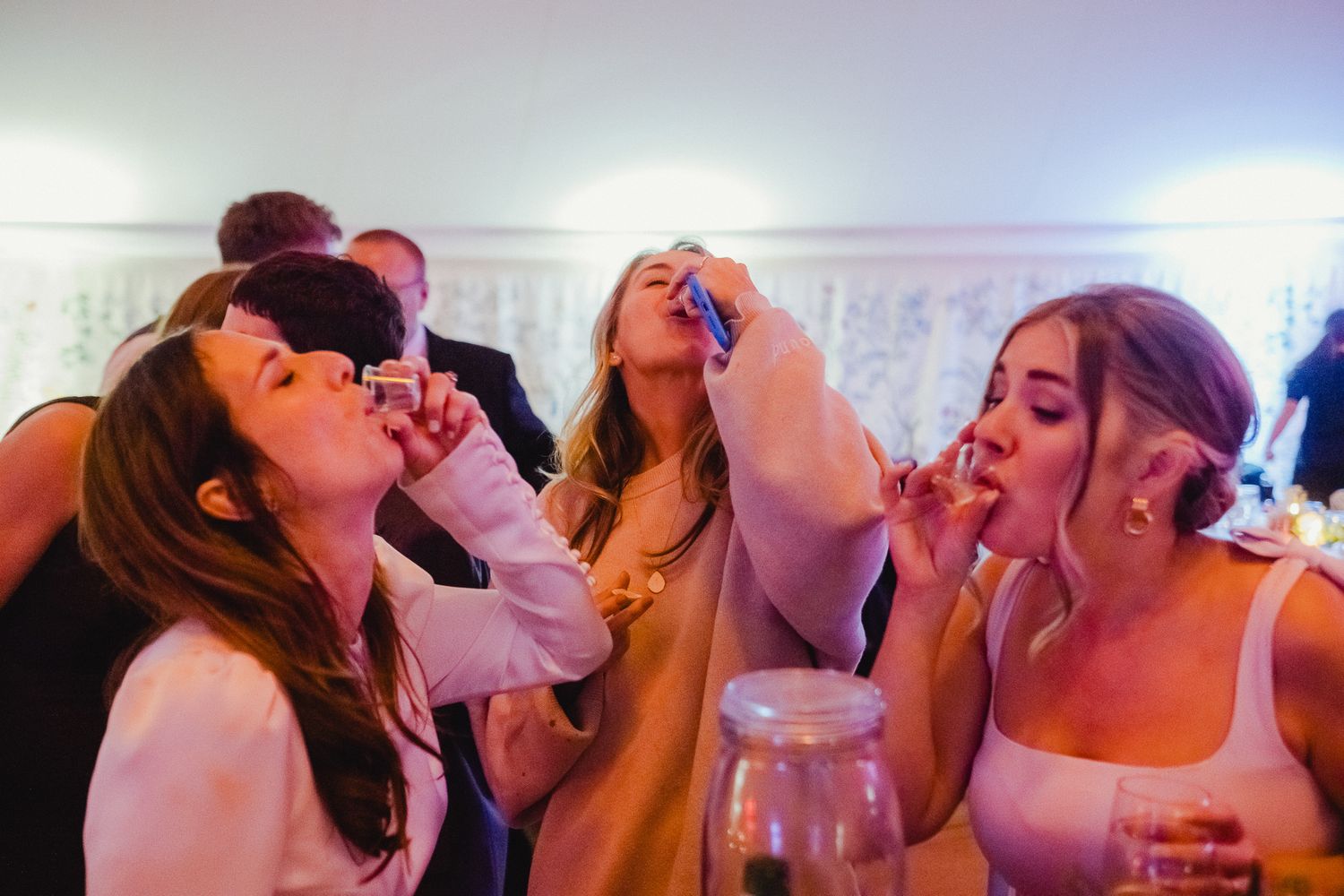 A group of people laugh and take shots together at a party under dim lighting.