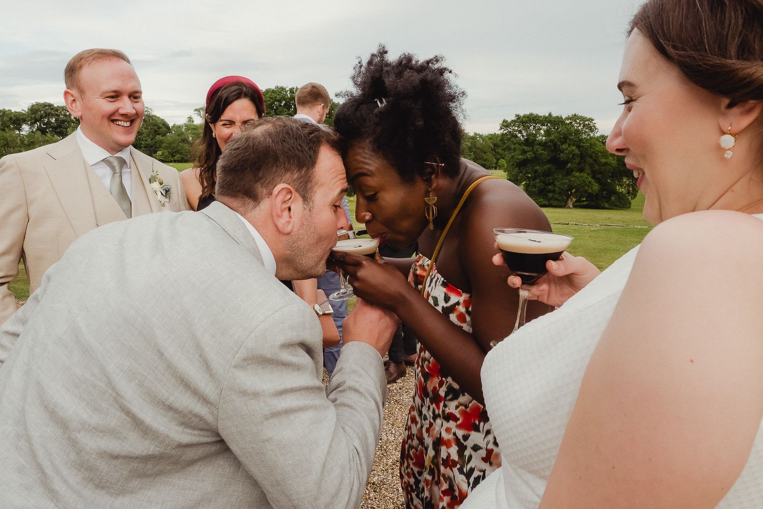 Wedding guests share joyful laughter during an outdoor celebration on a sunny day.