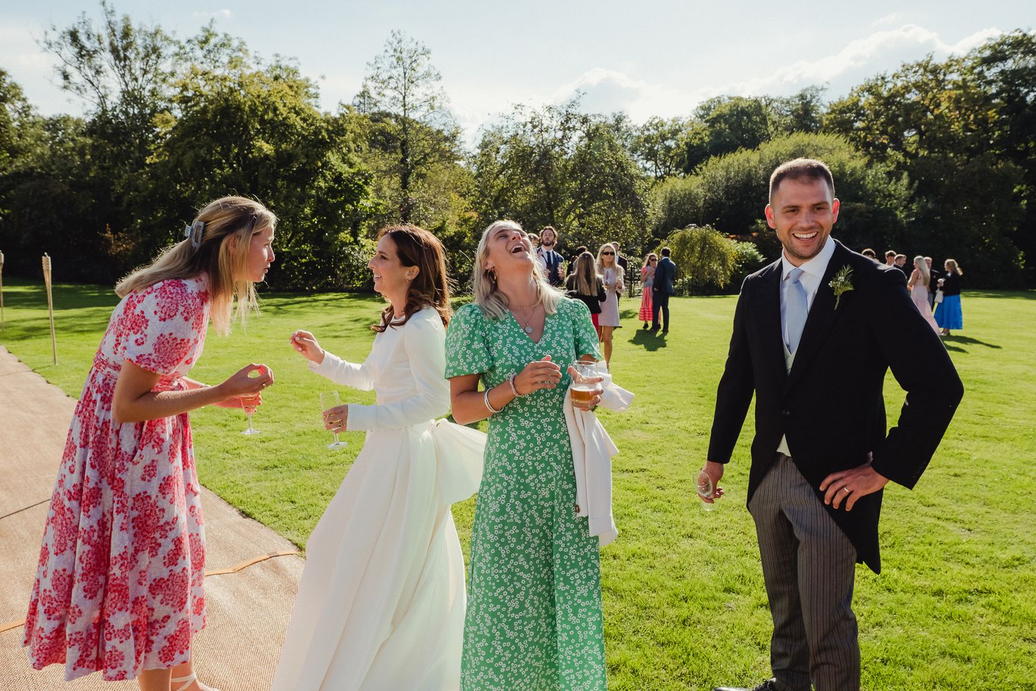 Wedding guests dancing and celebrating together on a sunny green lawn during an outdoor reception.