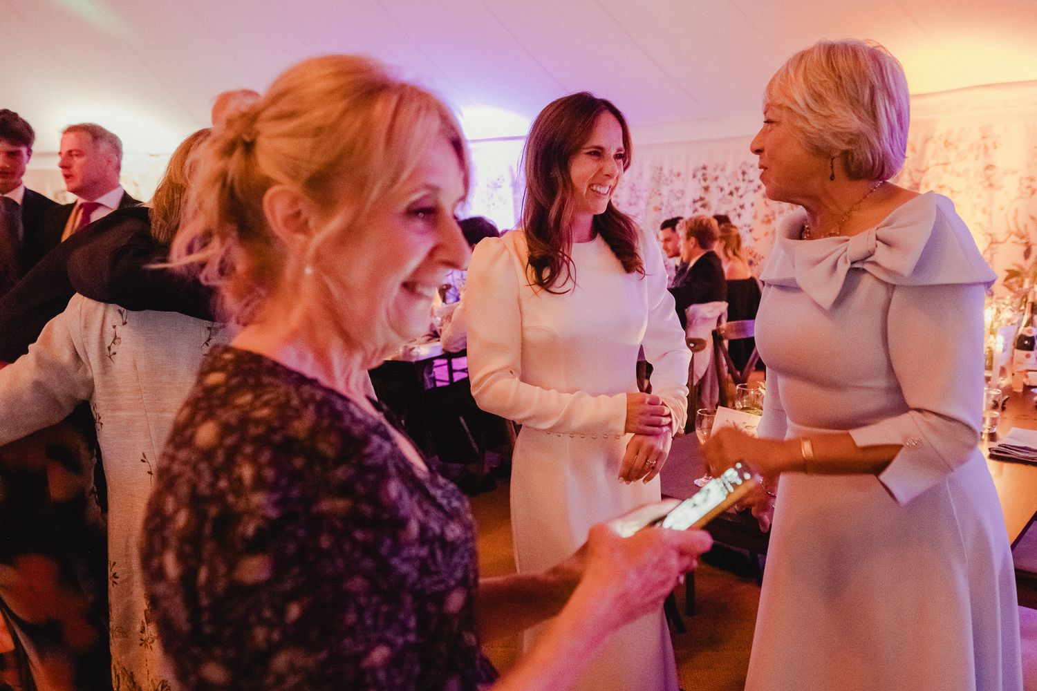 People gathered at an indoor event with pink lighting enjoying drinks and conversation.