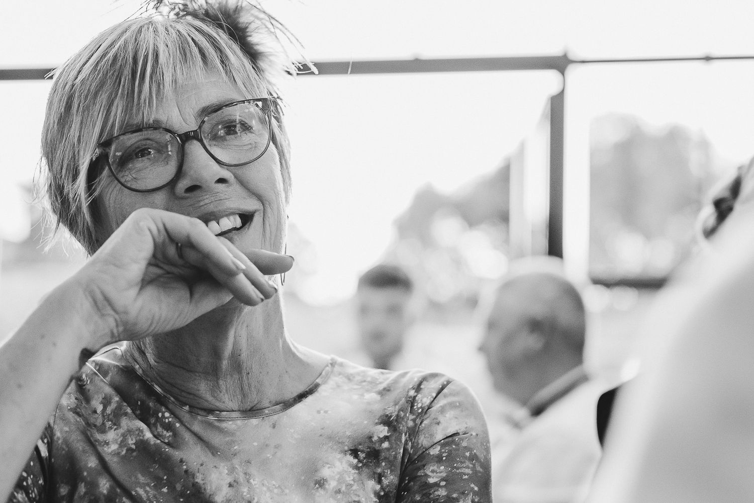 Black and white photo of someone wearing glasses and a floral print top laughing joyfully during a candid moment.