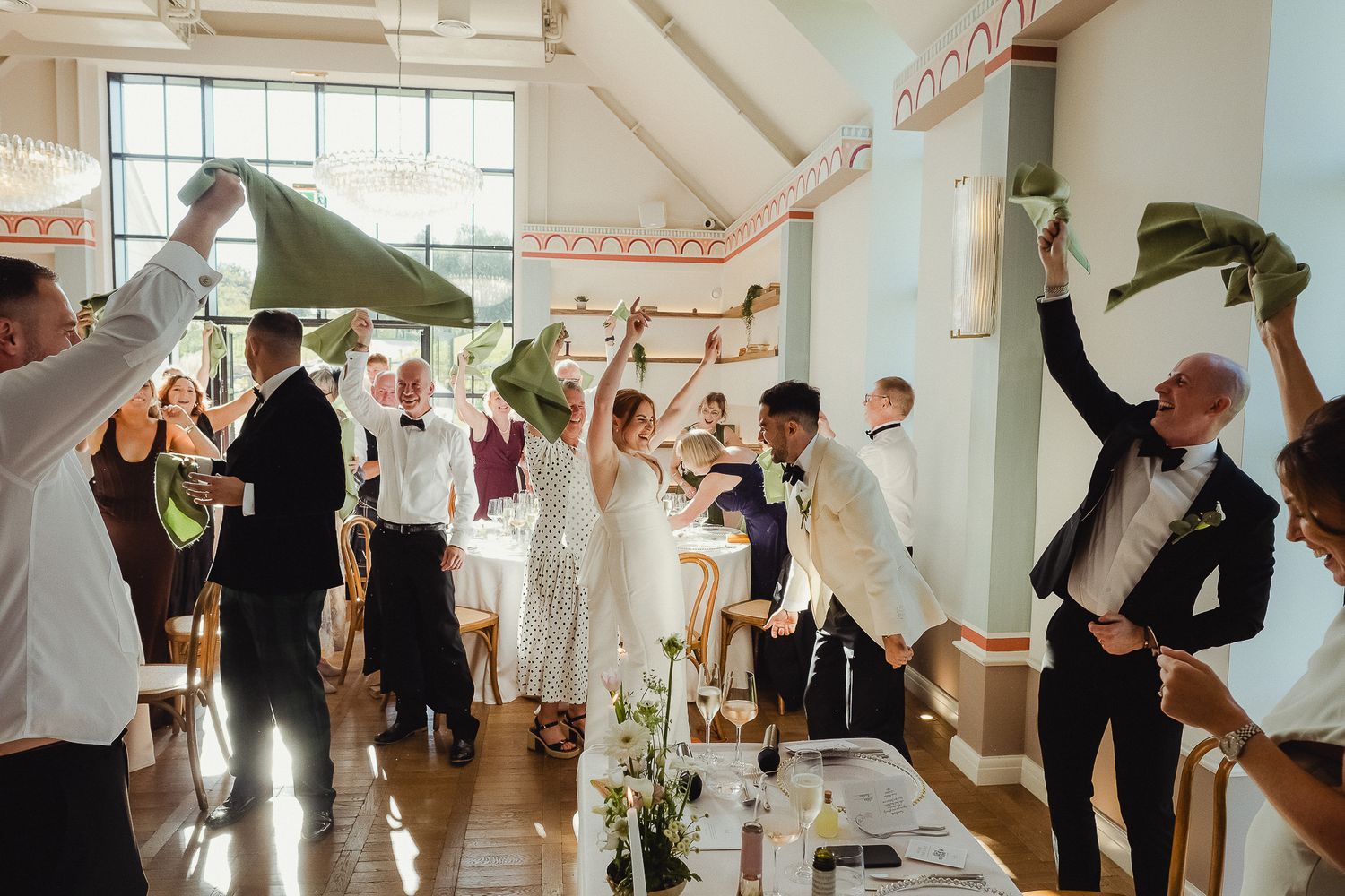 LIMEKILN Wedding Photography - guests wave green napkins in celebration during a bright reception in the sunlit Poplar Hall at LIMEKILN.