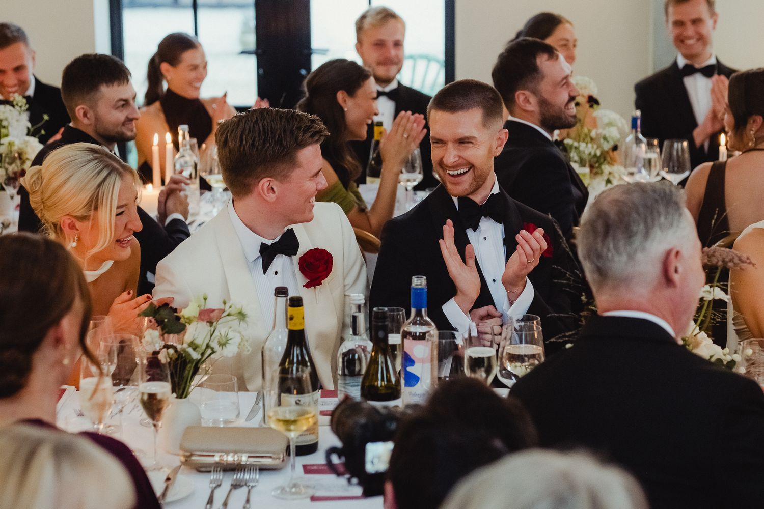 Guests share laughter and conversation at an elegant dinner reception with wine glasses and formal attire.