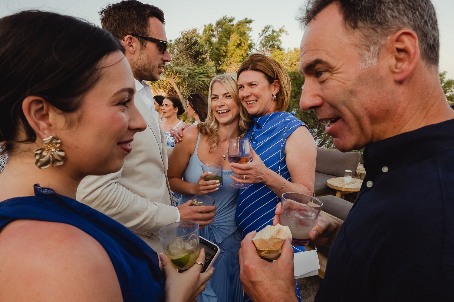 Friends gathered outdoors share joyful embraces and laughter during a sunny celebration.