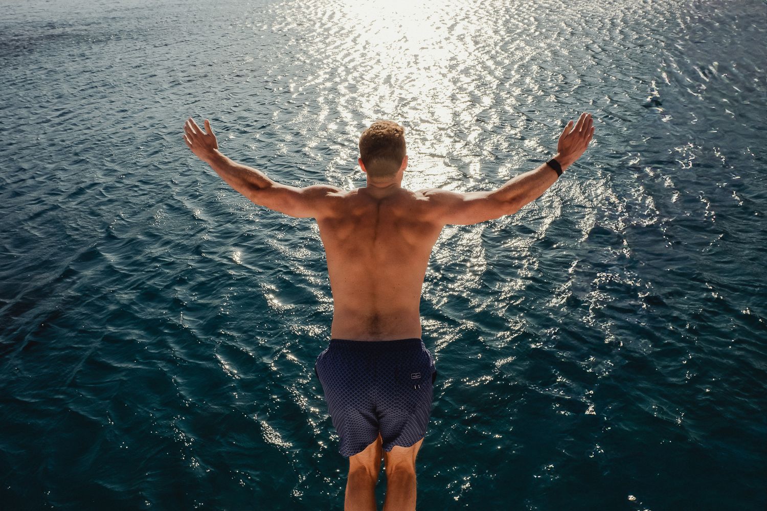 Person diving backwards into sparkling ocean water at dusk with arms outstretched in sequence of images.
