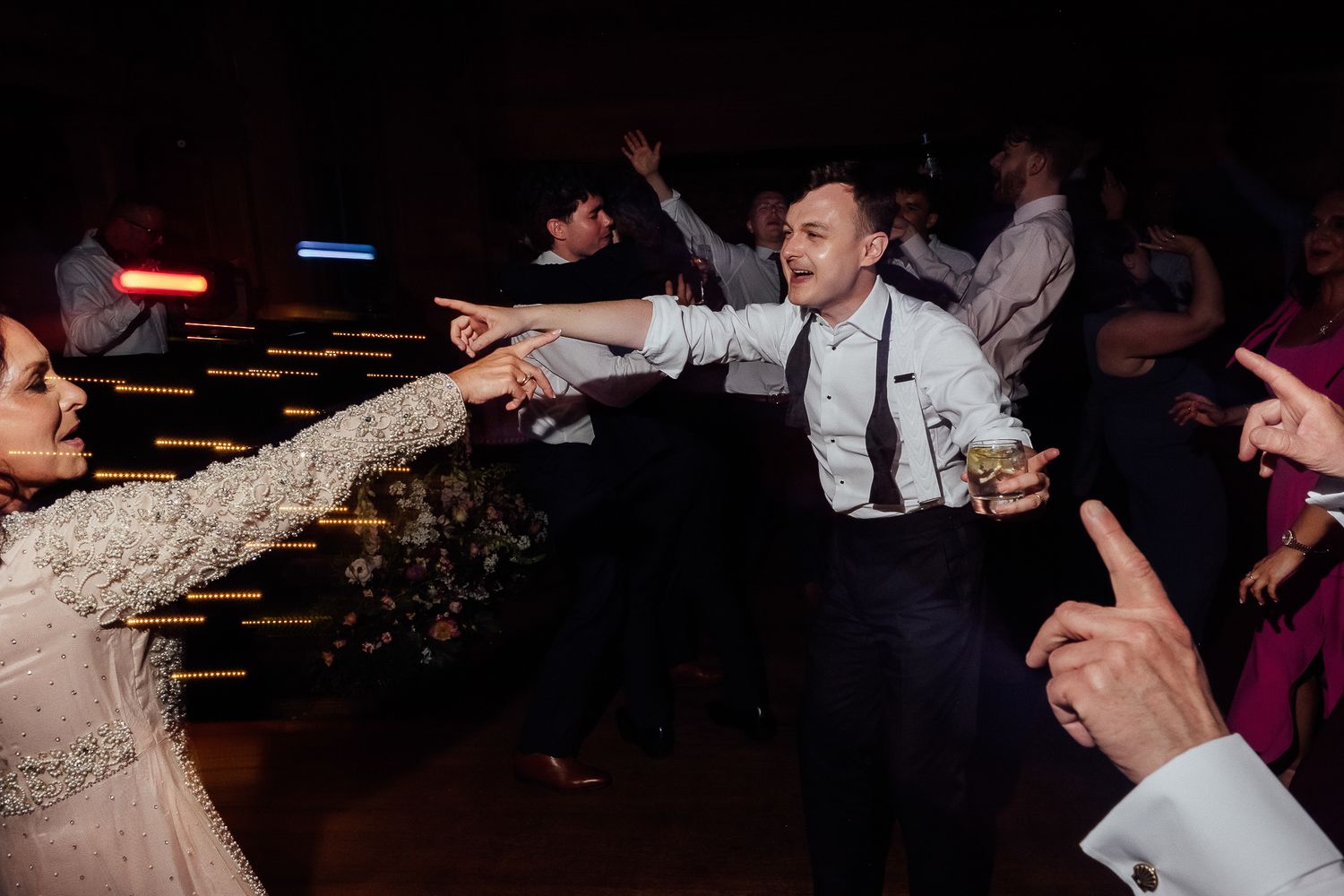 Groom dancing energetically with guests at a lively wedding reception party celebration.