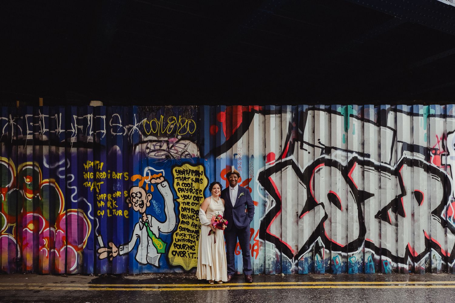 Colorful graffiti art decorates an urban wall with vibrant tags and designs under a dark overhang.