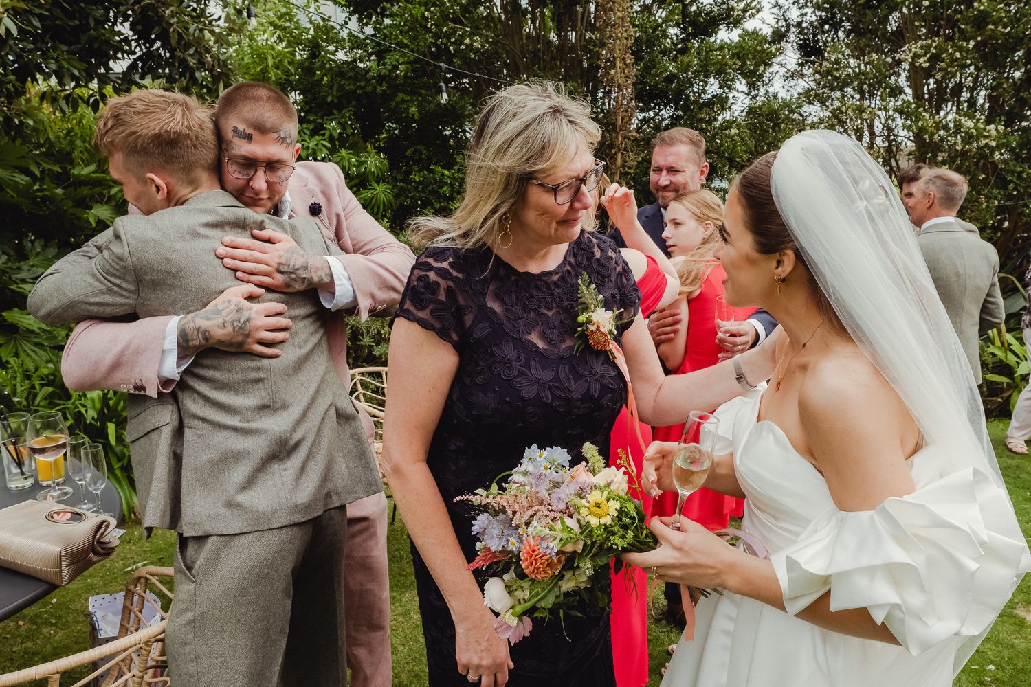 A group celebrates at an outdoor wedding reception with colorful flowers and joyful embraces.
