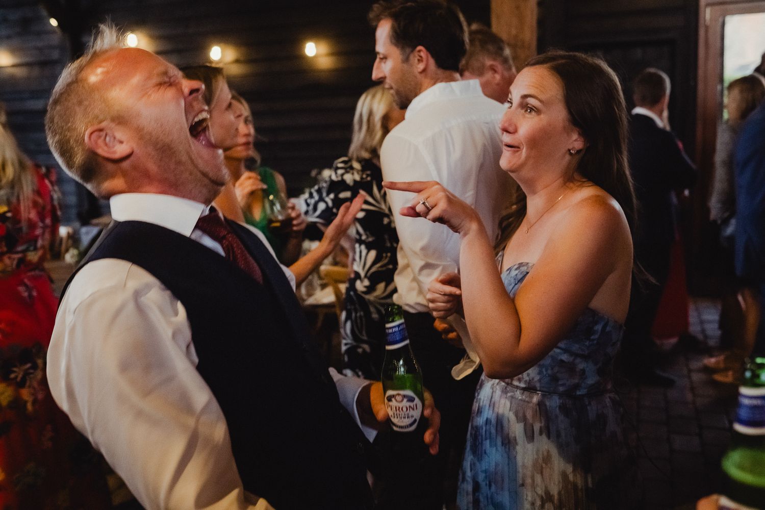 Wedding guests dance and celebrate on a dimly lit dance floor at an evening reception.