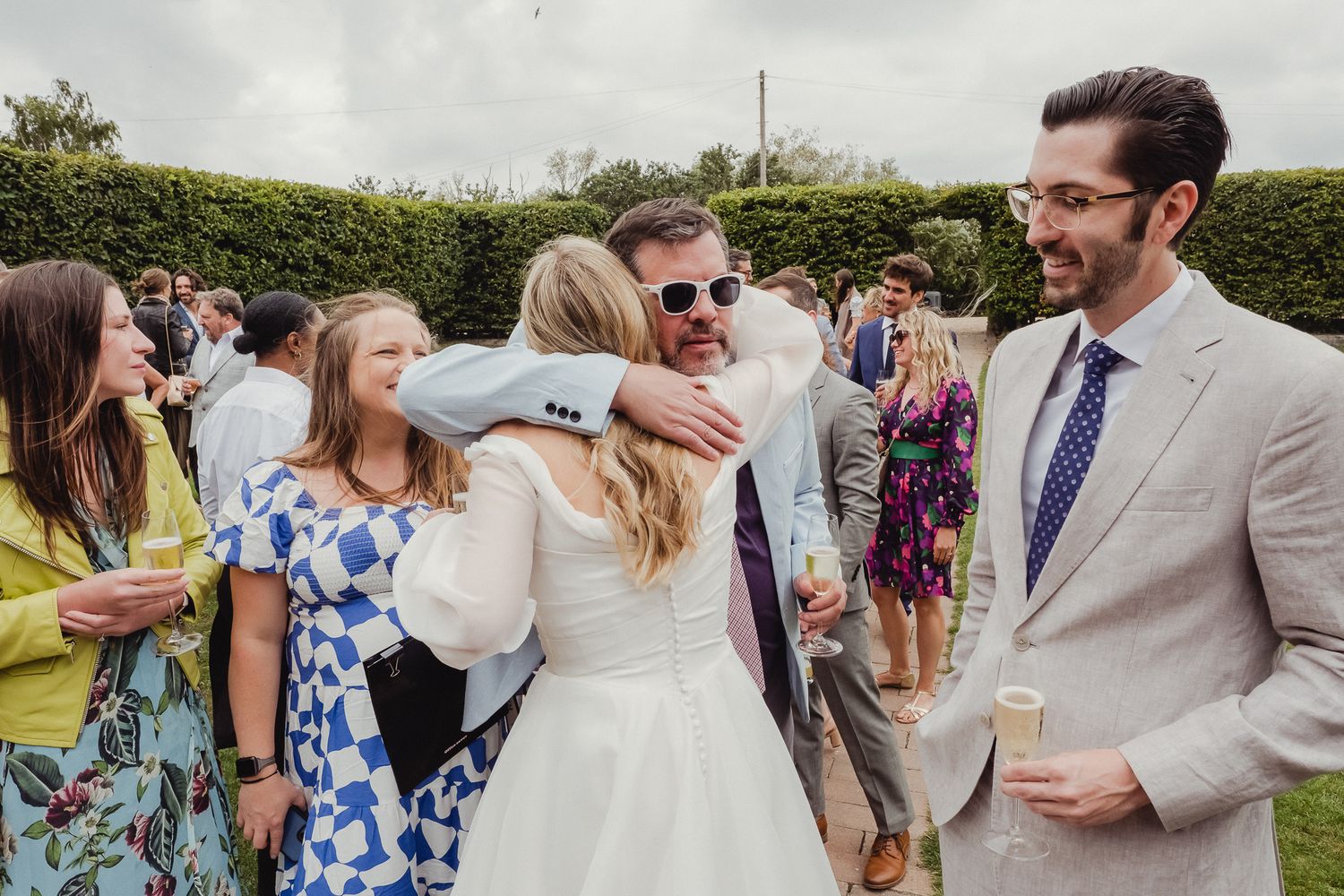 Wedding guests mingle and celebrate during an outdoor garden reception on a sunny afternoon.