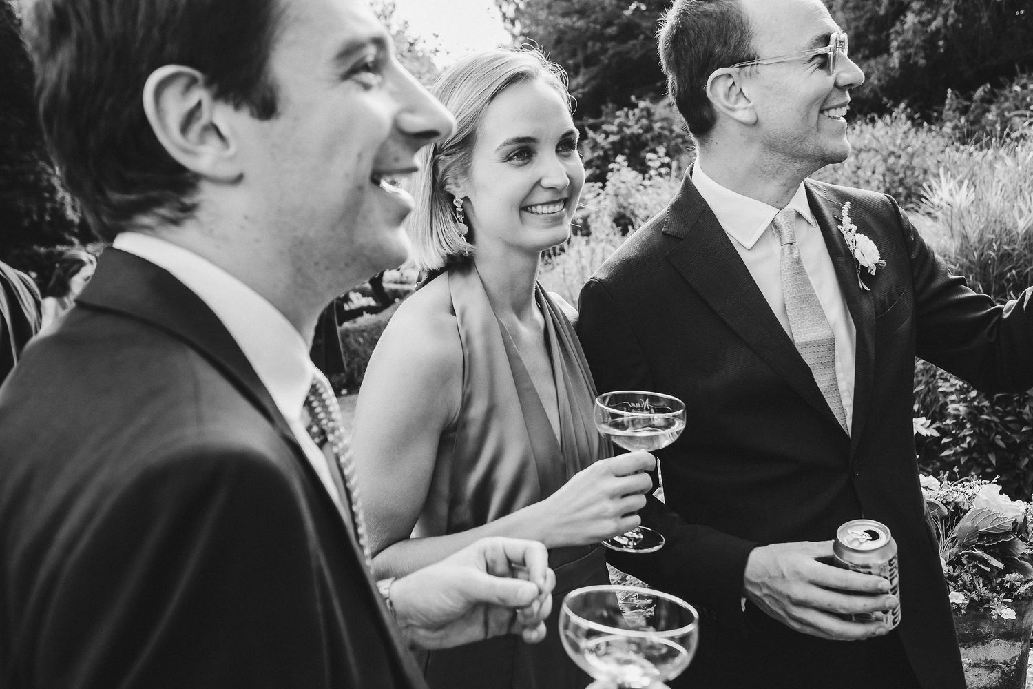 A black and white photo of wedding guests enjoying drinks and conversation outdoors.
