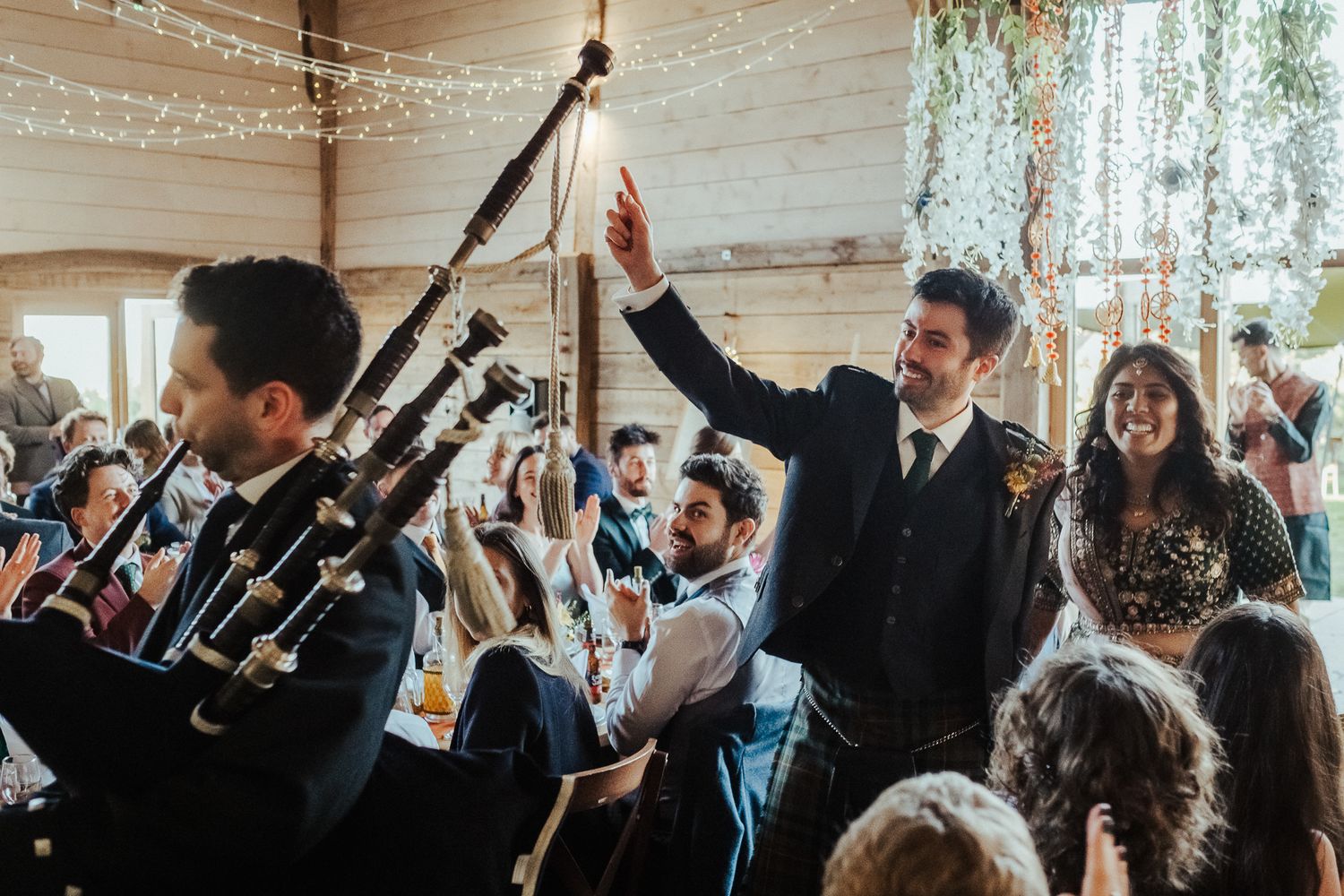Celebratory moment at a wedding reception with bagpipes and guests raising their hands in joy.