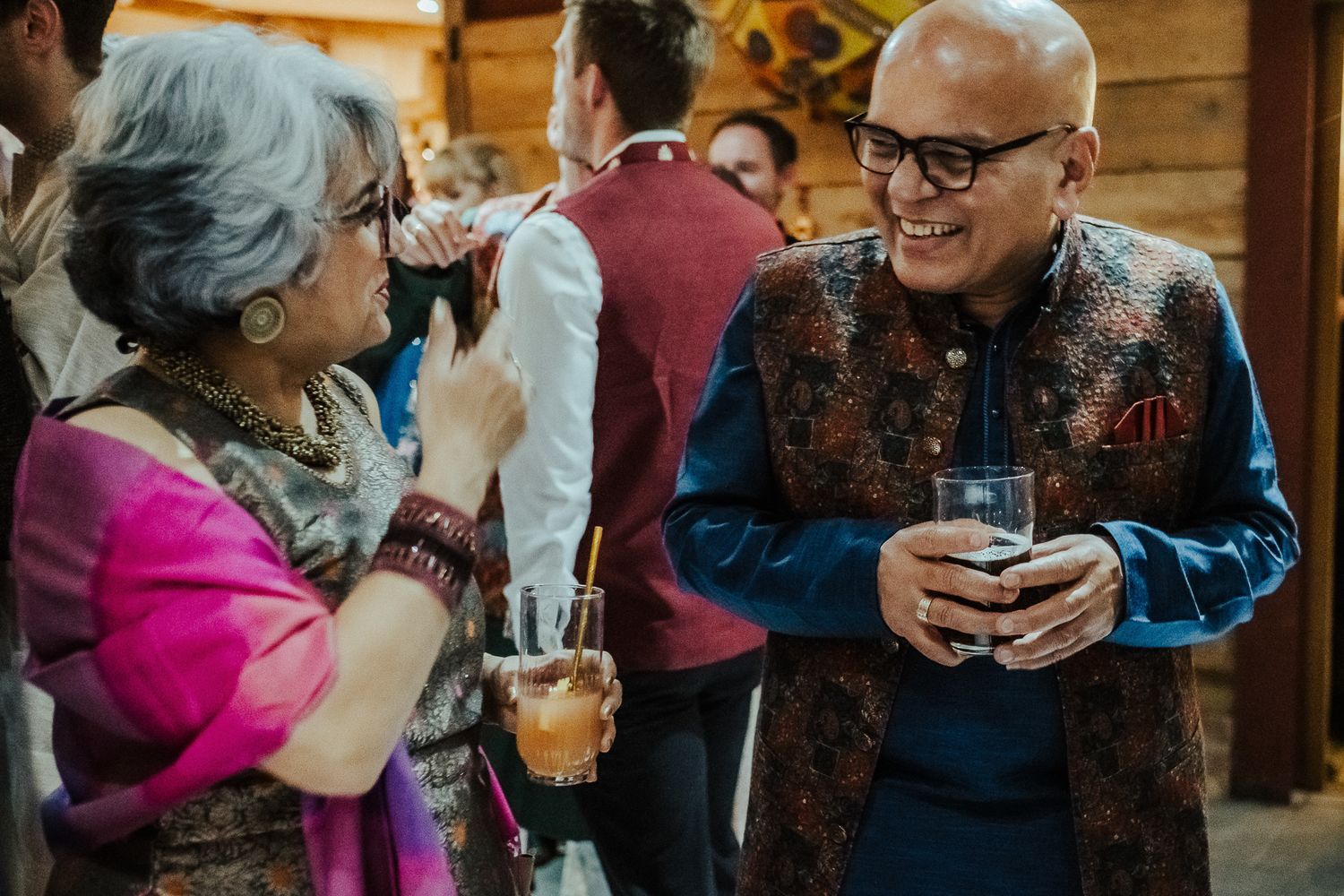 Two guests engaged in animated conversation at a social gathering while holding drinks.