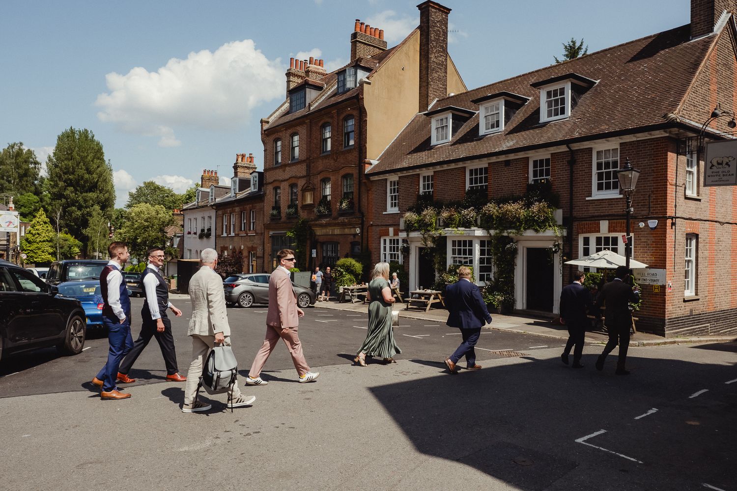 People walking along a historic cobblestone street with traditional brick buildings and shops in an English village.