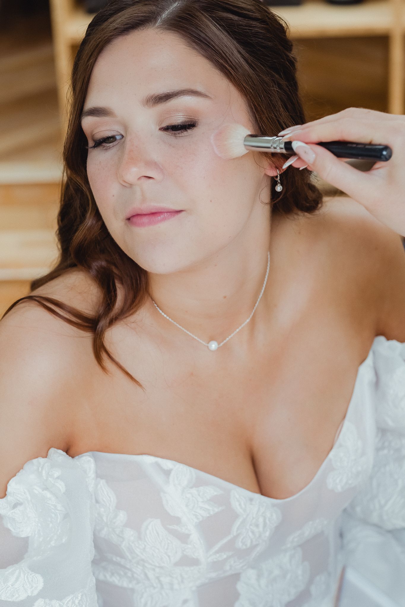 Professional makeup artist applies finishing touches to bride's delicate eye makeup during wedding preparation.