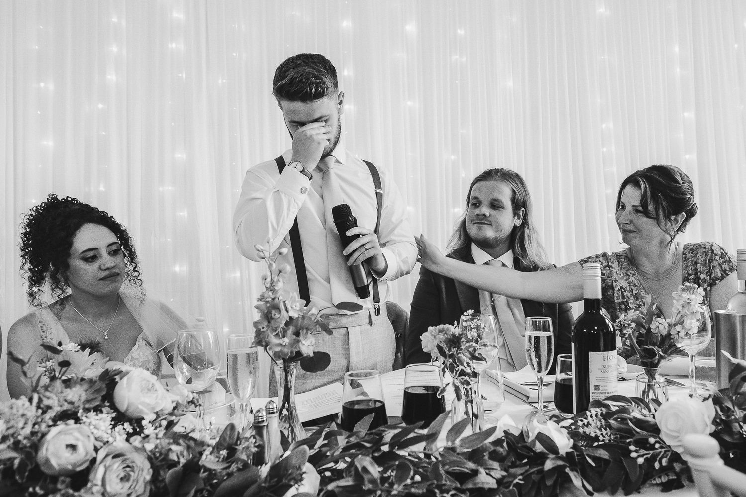Black and white photo of wedding reception guests seated at long tables enjoying a celebration meal together.