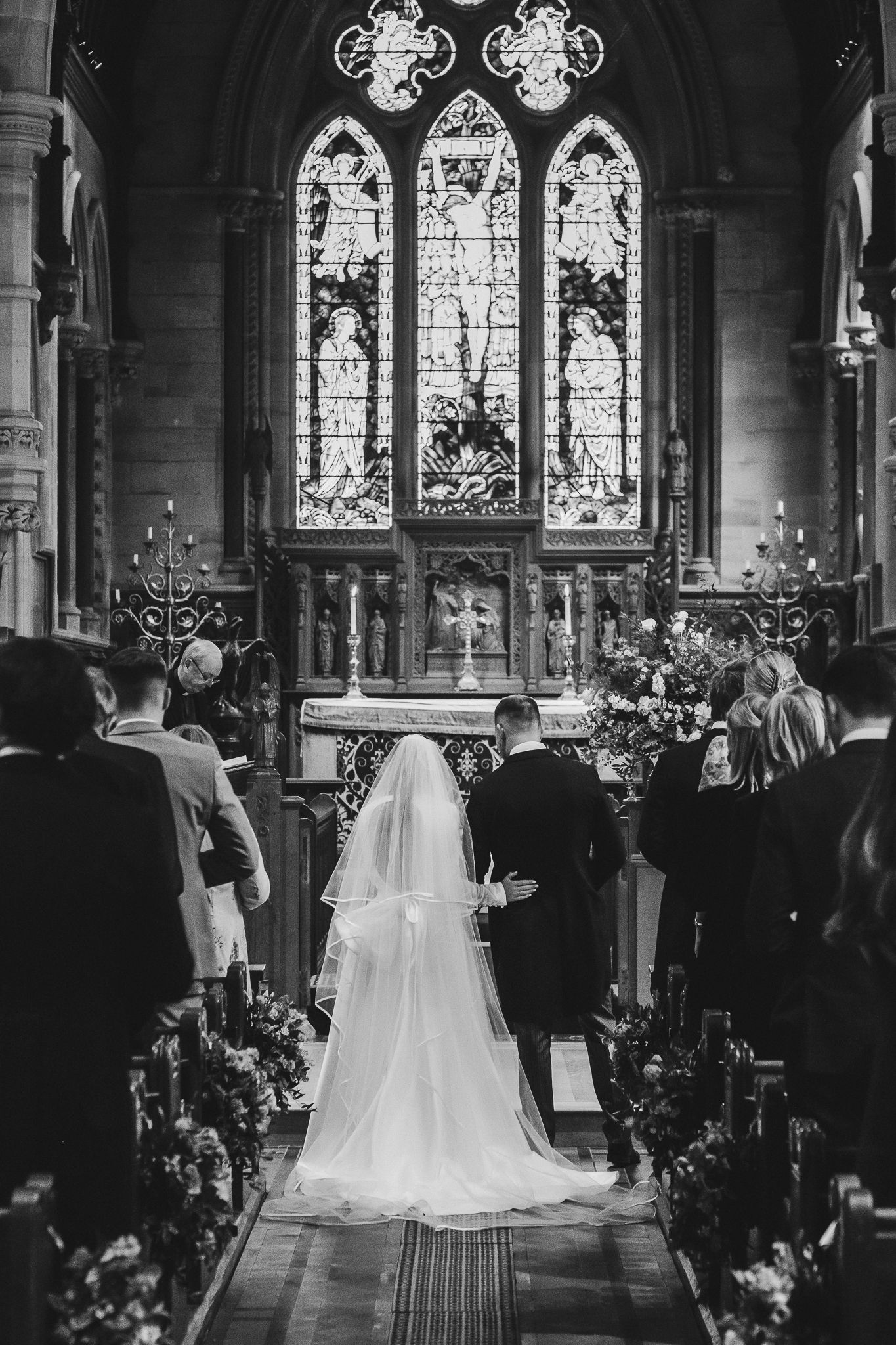 Black and white wedding ceremony photos showing couple at altar in traditional church with stained glass windows and floral decor.
