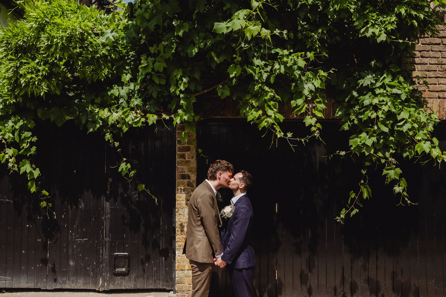 A couple shares a romantic kiss under lush green trees in a garden setting.
