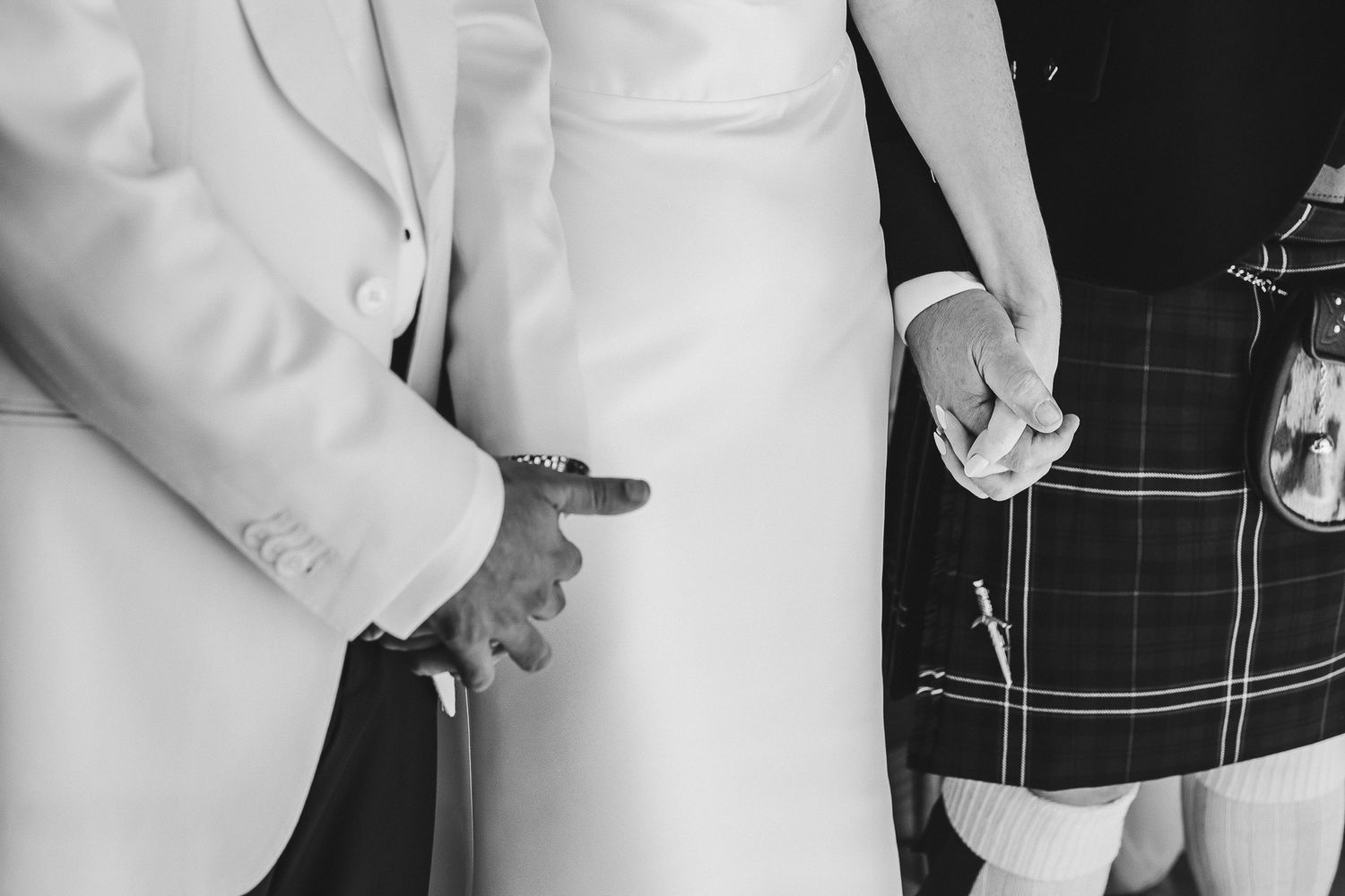 A close-up view of hands adjusting a formal white suit jacket sleeve during a wedding preparation.