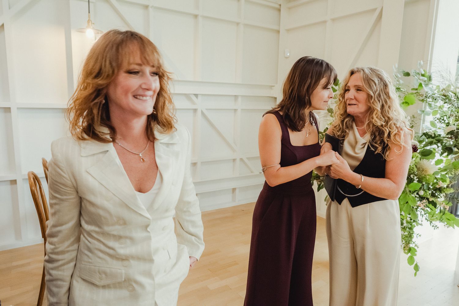 People sharing warm hugs and emotional moments during what appears to be a wedding reception in a white room.