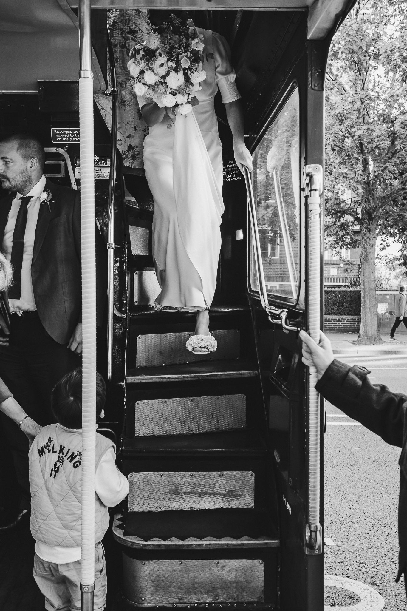 Black and white photograph showing someone ascending stairs in a wedding dress while holding a bouquet.