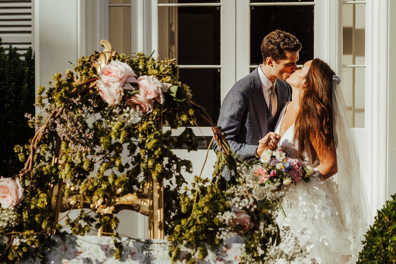 Newlyweds share a romantic moment under a floral arch decorated with pink roses.