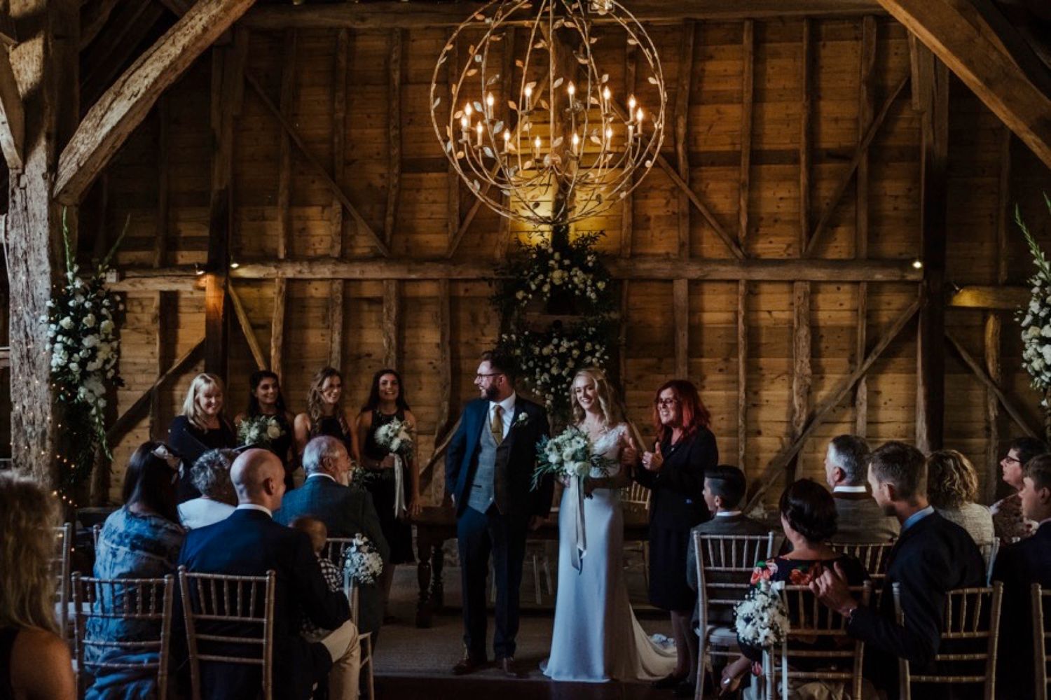 Rustic barn wedding ceremony setup with wooden beams and elegant chandeliers.