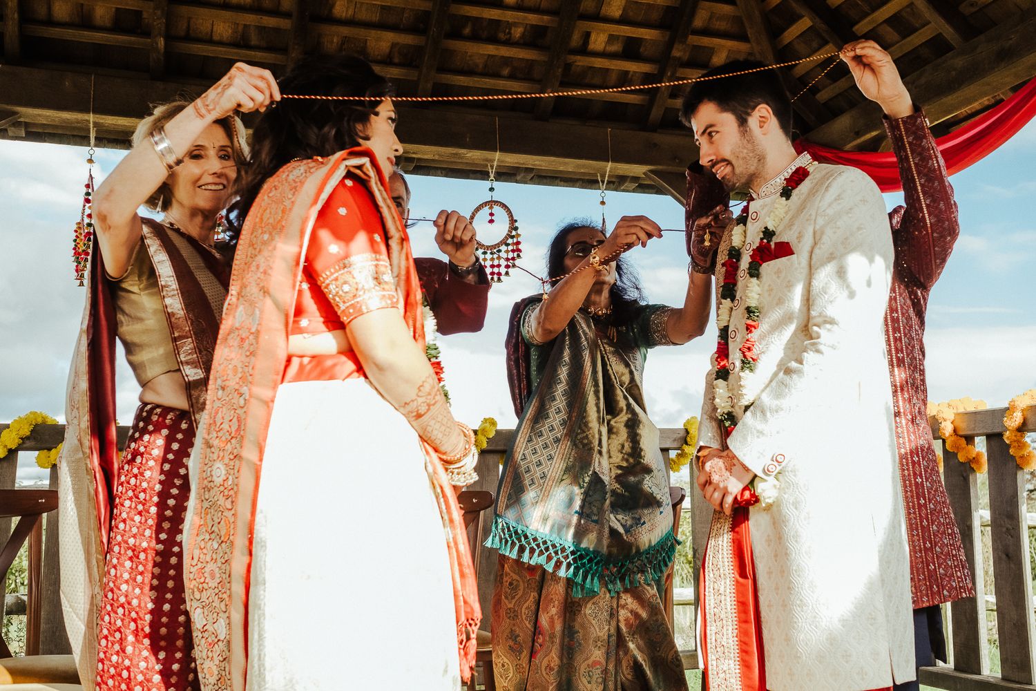 A traditional Indian wedding ceremony takes place under a covered outdoor pavilion with vibrant decorations.