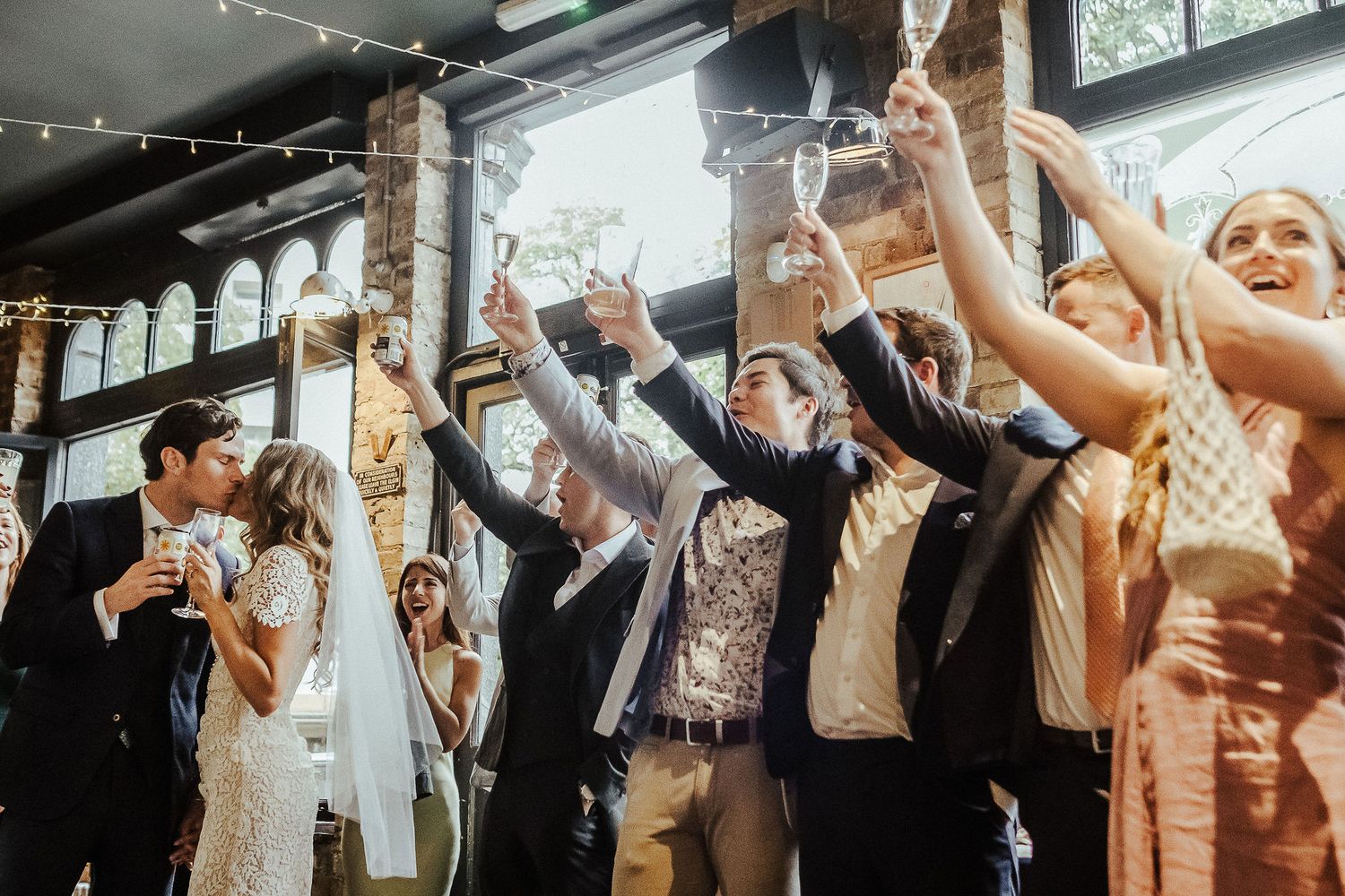 A lively crowd of wedding guests dance with raised arms on a packed dance floor during a reception celebration.
