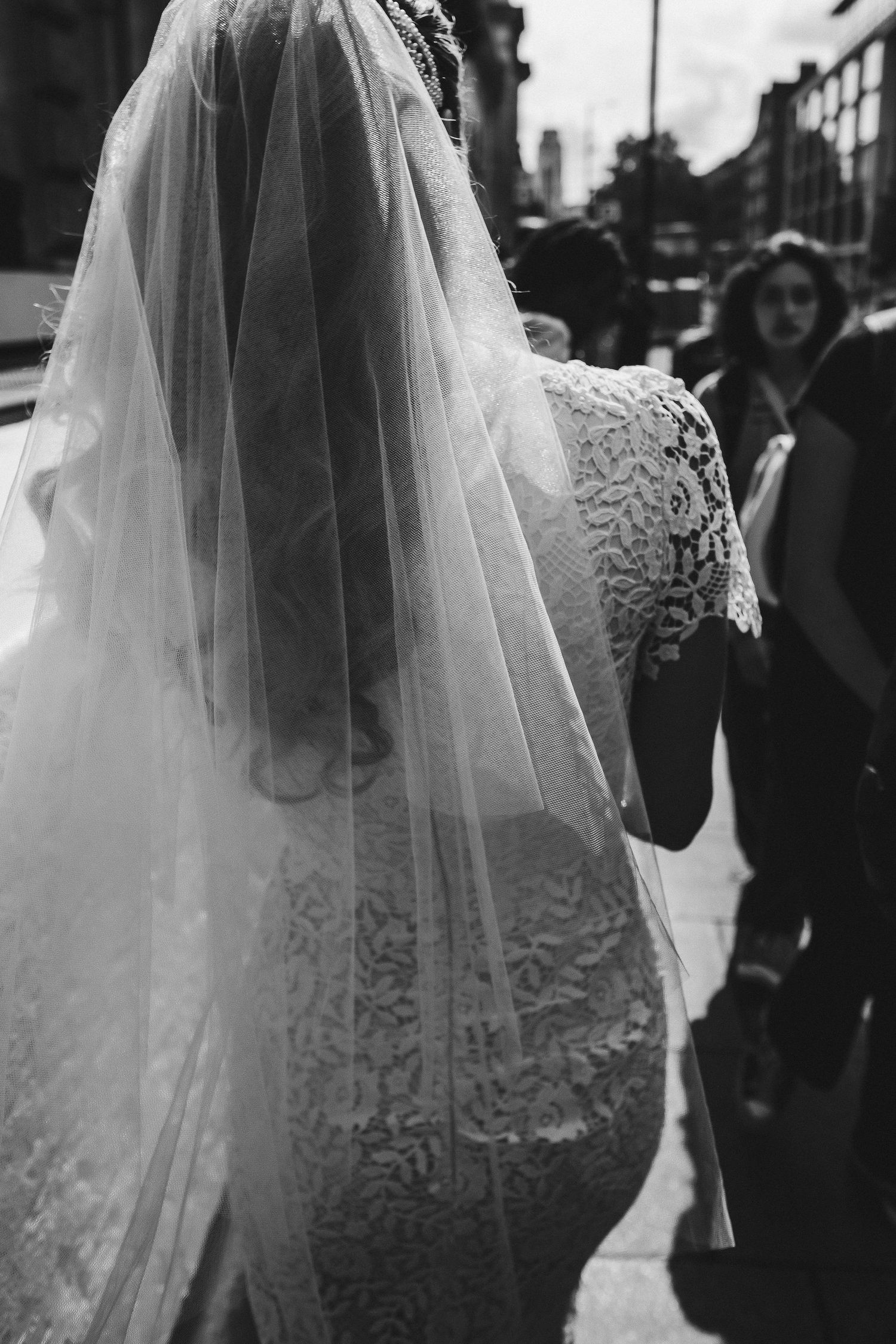 A series of black and white wedding photos showing the back details of a bride's lace dress and flowing veil.