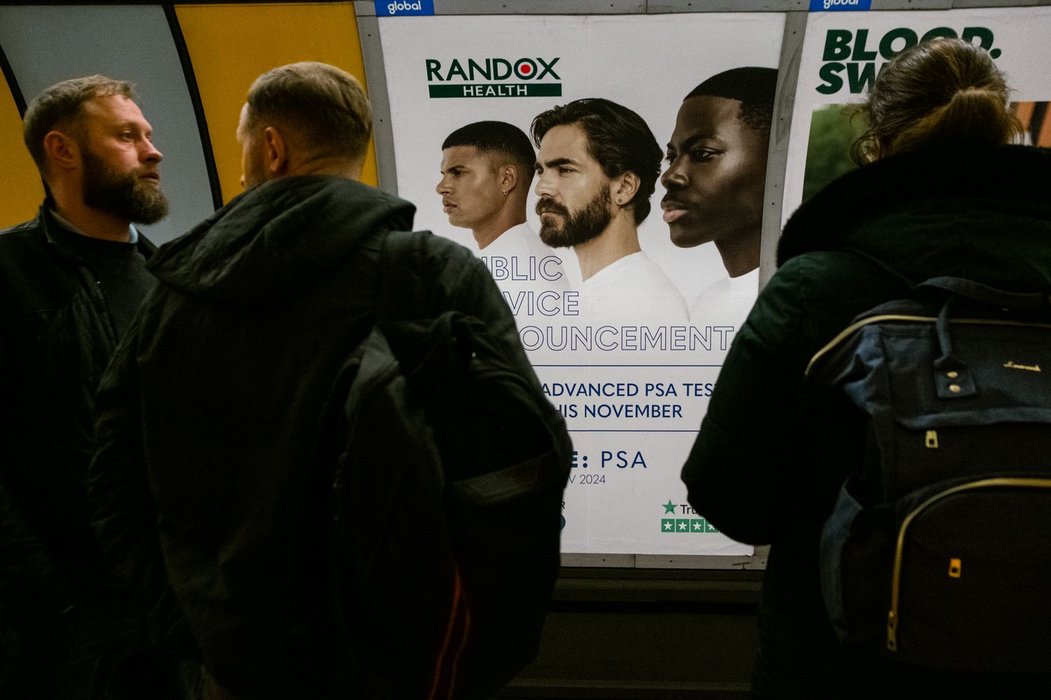 A group of people stand together in a dimly lit space with signs and posters visible on the wall behind them.