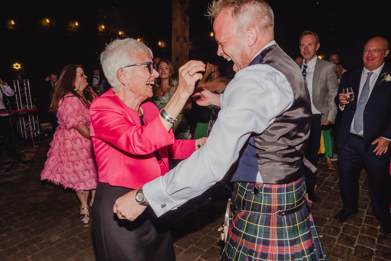 People dancing together at a festive evening celebration on a brick patio with ambient lighting.