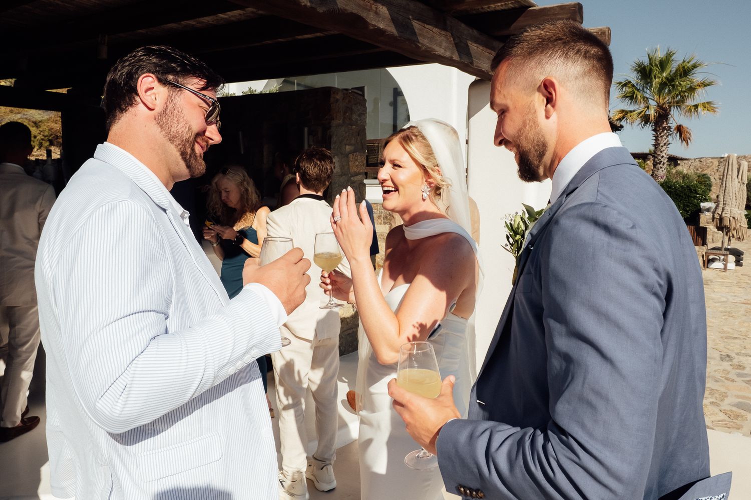 Wedding guests laughing and toasting with champagne at an outdoor beach wedding reception.