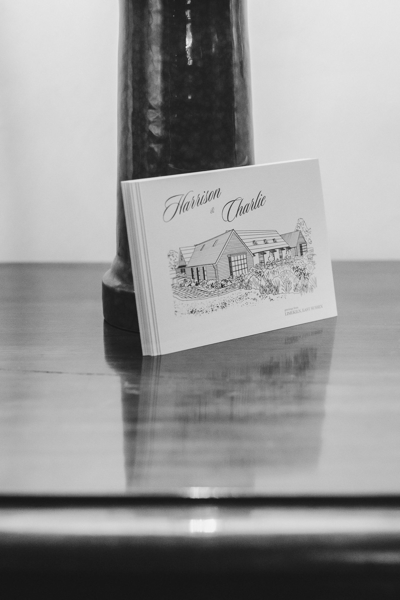 Black and white photograph of business cards with architectural sketches displayed in a row on a reflective surface.