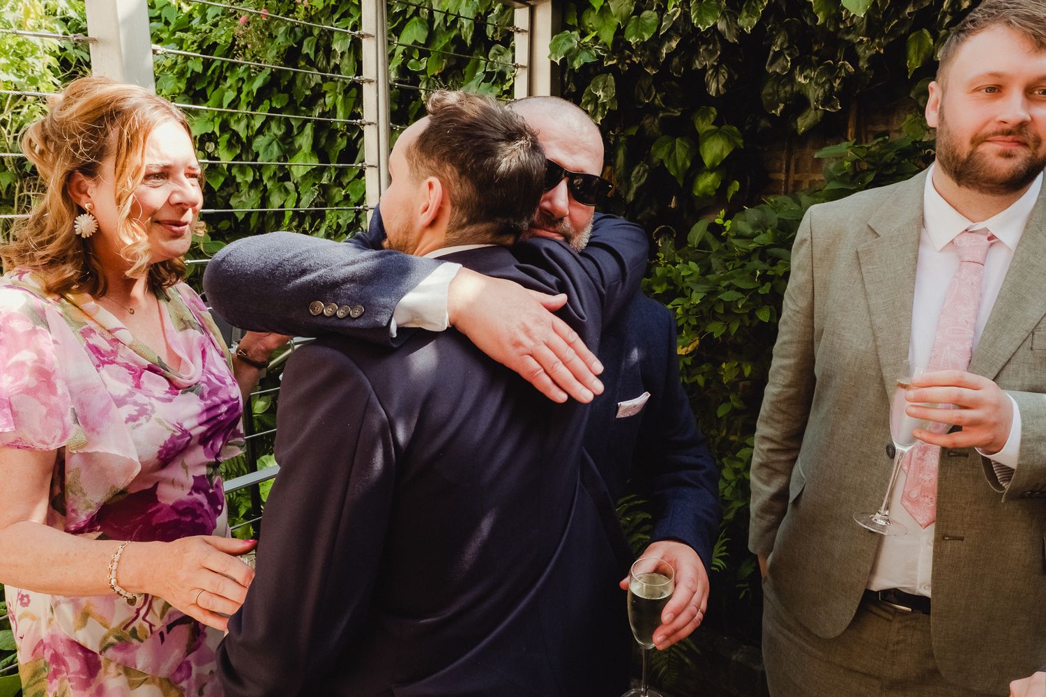 Wedding guests embrace and celebrate during an outdoor garden reception.