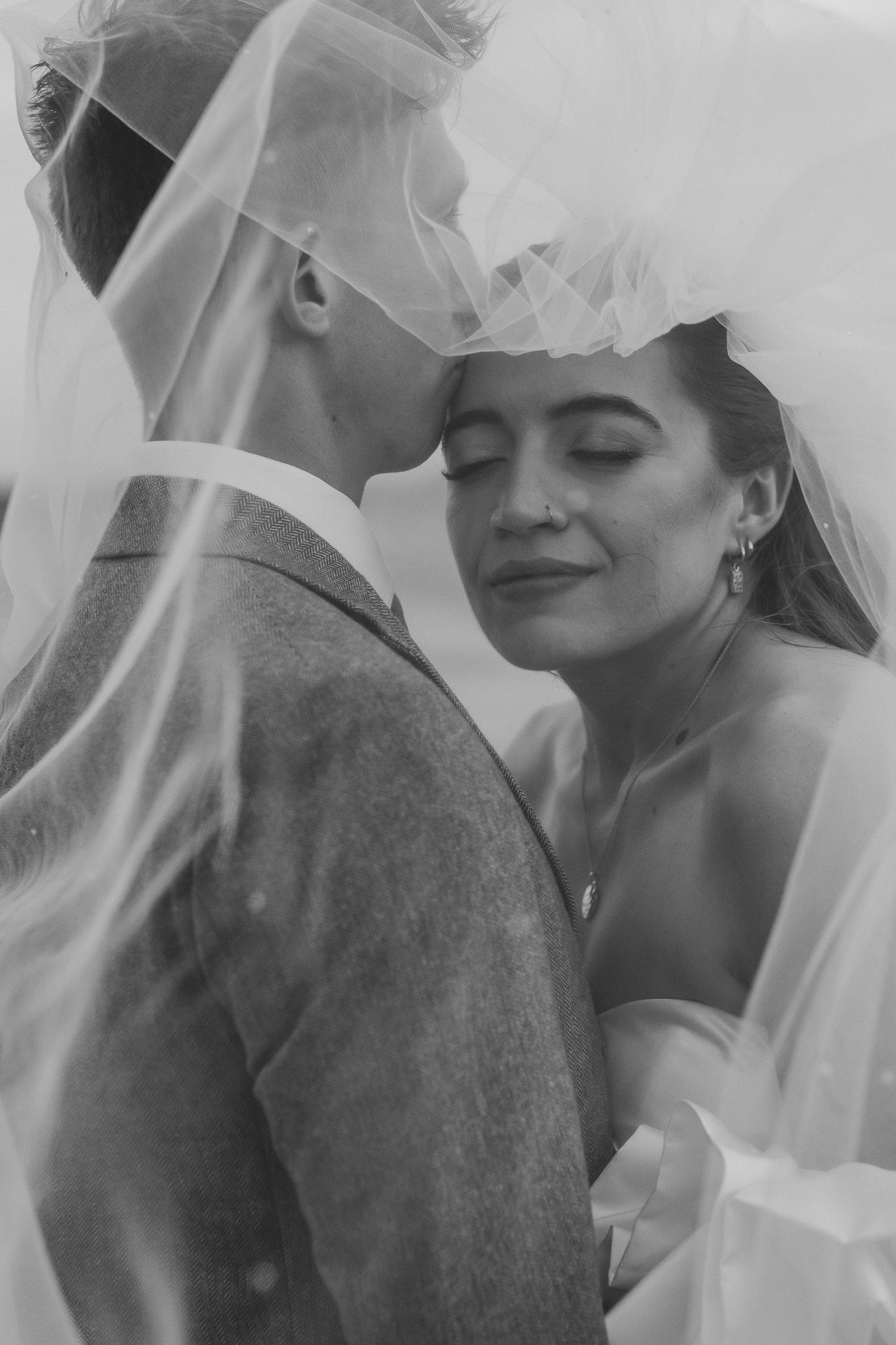 A romantic black and white wedding photo series showing tender moments between newlyweds through a flowing veil.