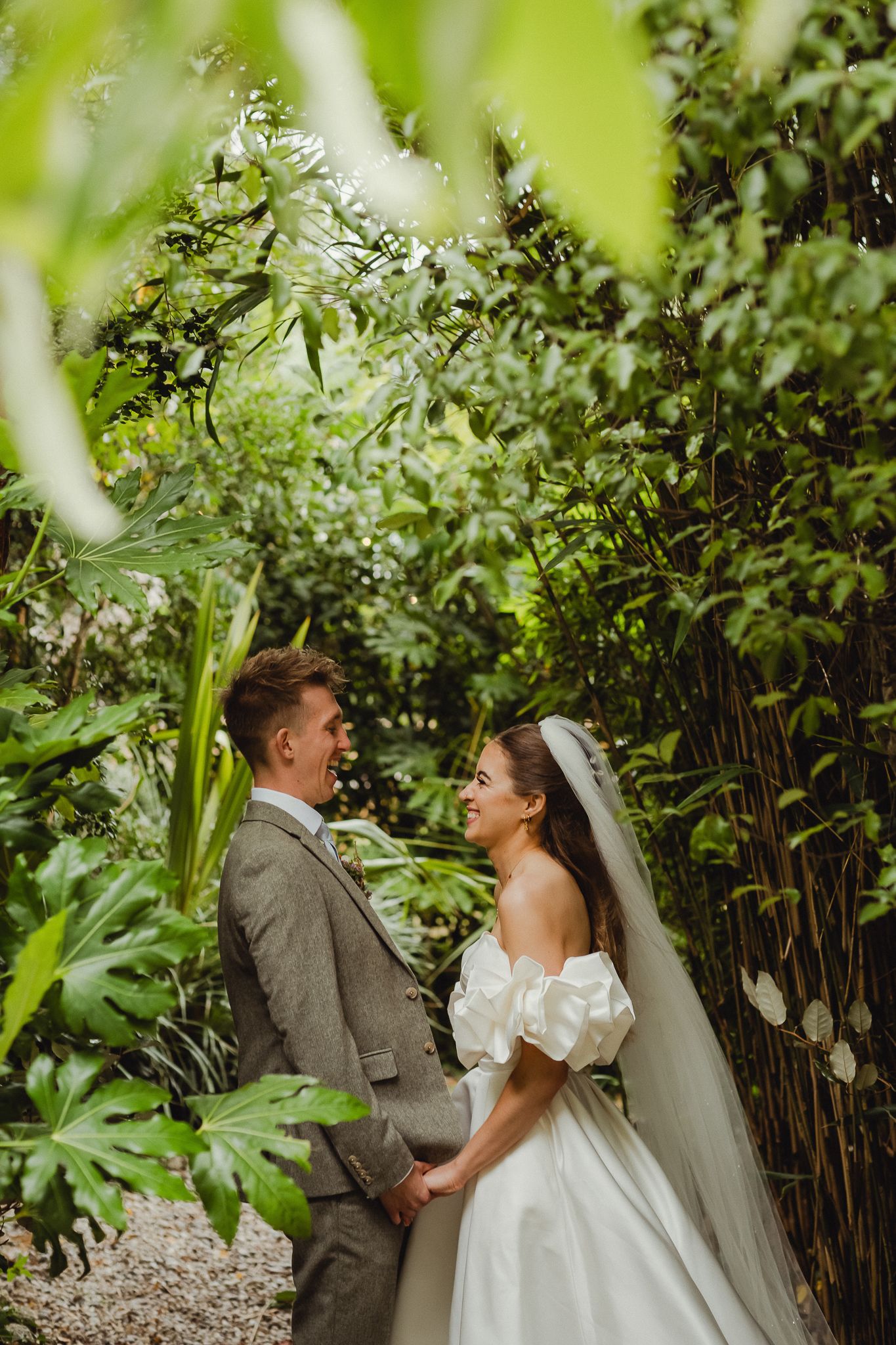 A couple shares a joyful moment surrounded by lush bamboo and greenery in a garden wedding setting.