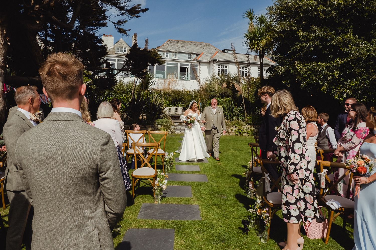Wedding guests line up to throw confetti at a garden ceremony on a sunny summer day.