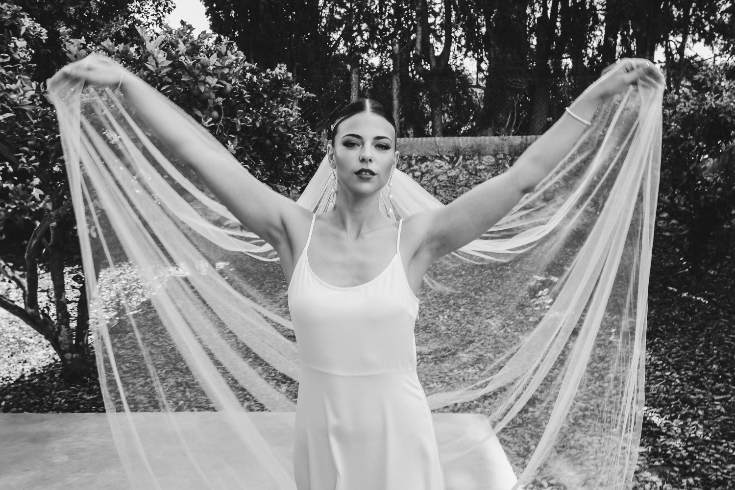 A black and white photo series showing a flowing bridal veil being dramatically tossed in an outdoor garden setting.