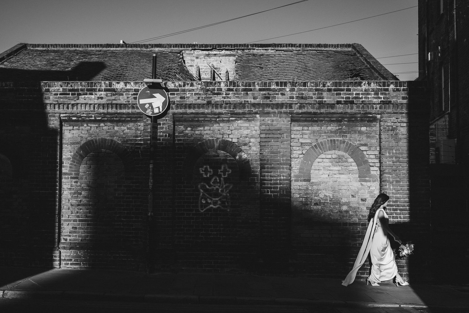 Black and white architectural photograph showing a brick wall with dark shadows and contrasting light patterns.