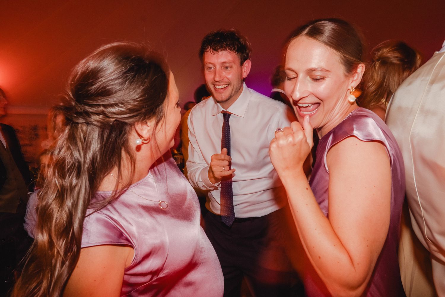 Group of people dancing and laughing together at a party with red lighting in the background.