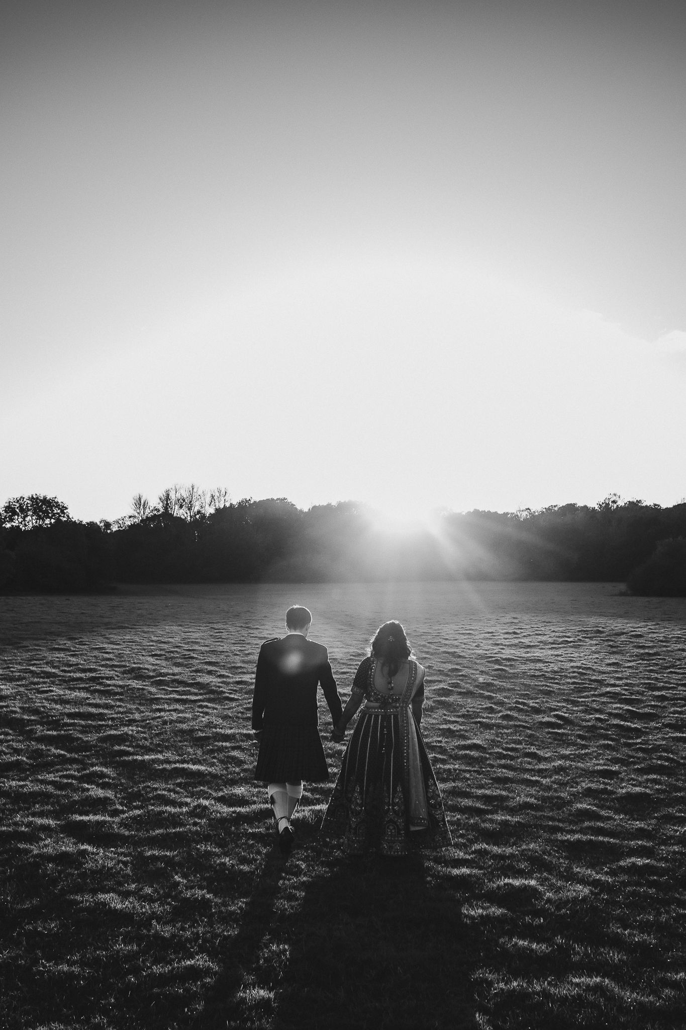 Silhouette of couple walking hand in hand across a field at sunset.