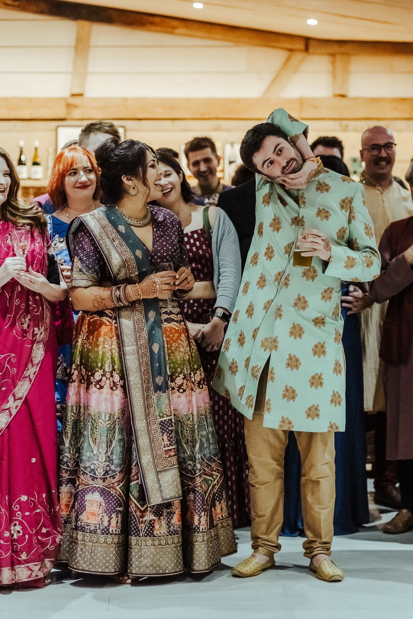 Group of guests in colorful traditional Indian attire laughing together at a celebration.