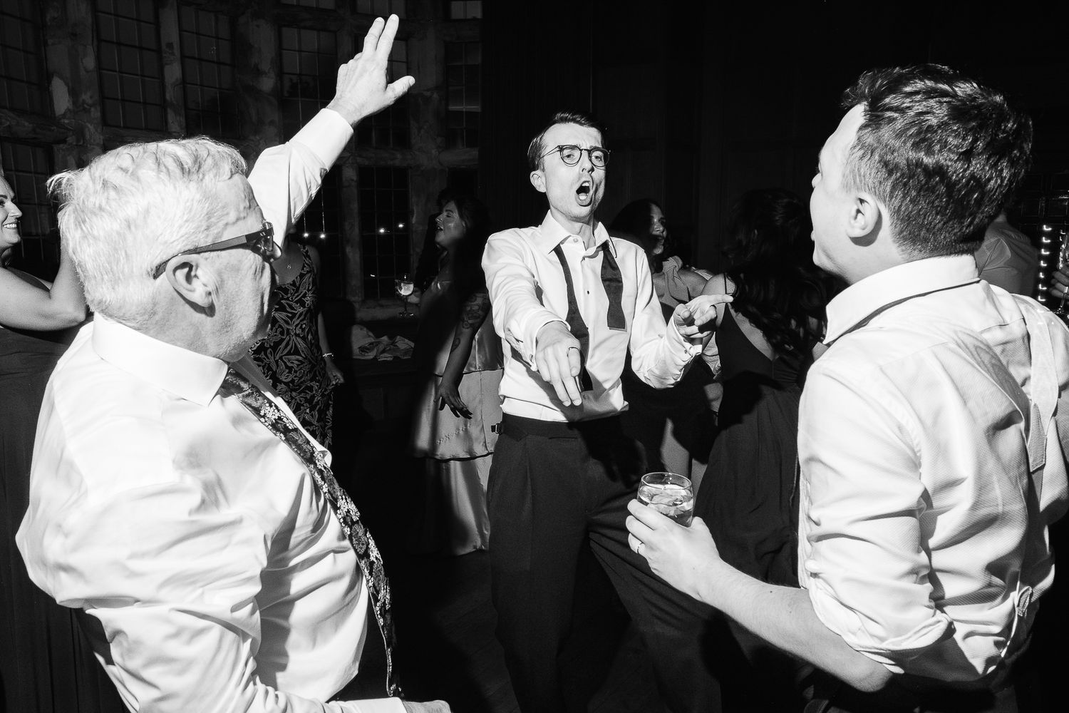 Black and white photo of guests dancing and celebrating joyfully at a wedding reception party.